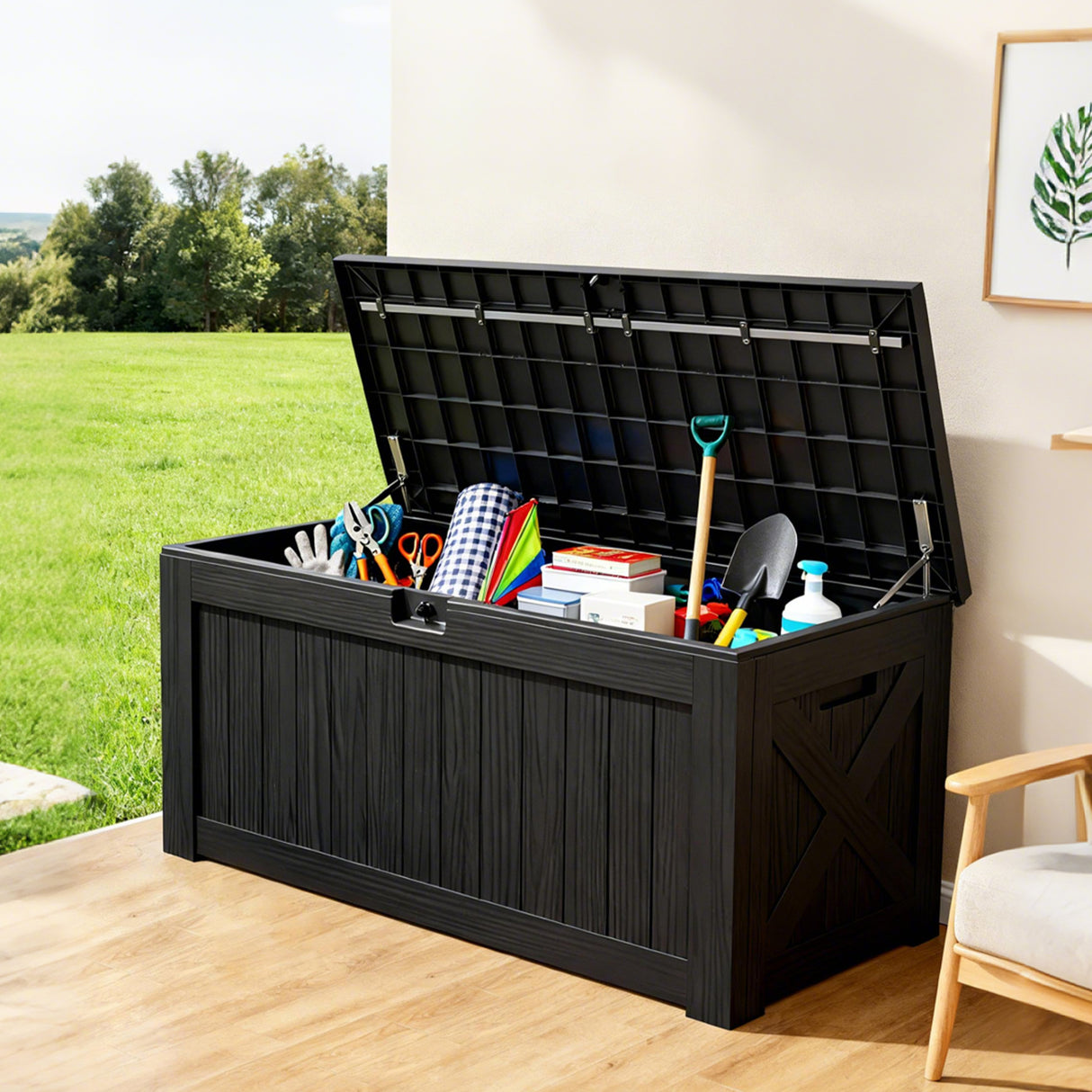 Large black outdoor deck box with open lid storing garden tools and household items, lockable resin storage box