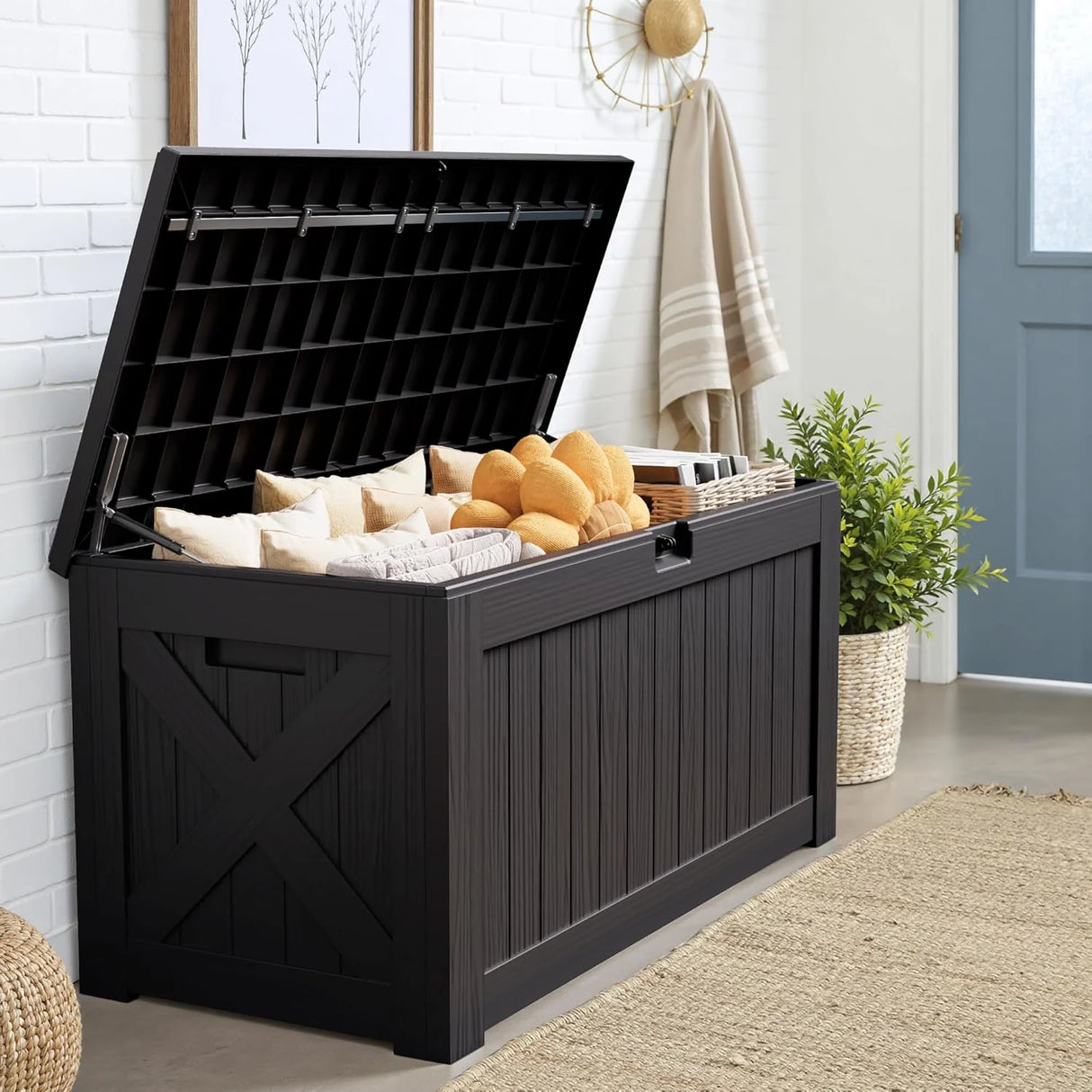 Outdoor deck box with open lid storing cushions and pool towels, large black resin weatherproof patio storage box