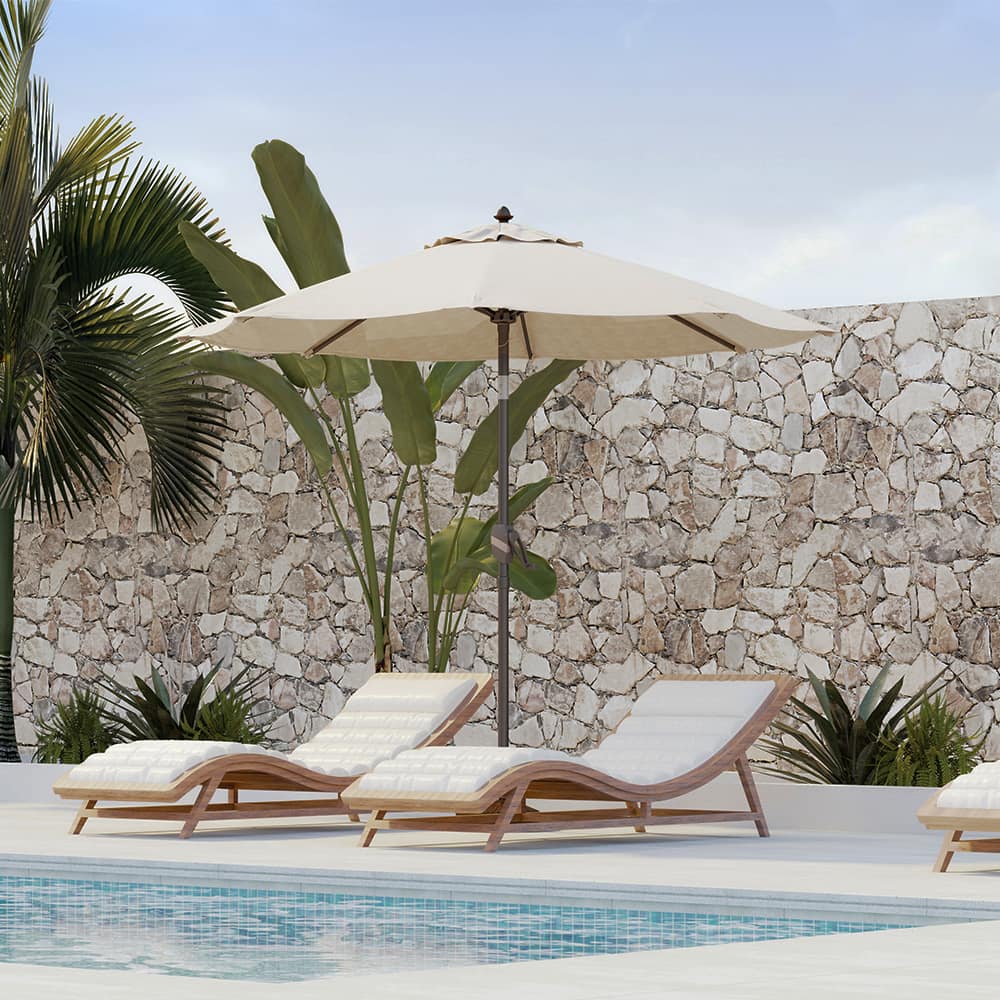 Patioslife Solara cream market umbrella shading poolside loungers with tropical plants and stone wall backdrop