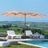 Patioslife Horizon Haven double-sided patio umbrella with base in tan, 4.6 x 2.7m,with LED lights shading a modern outdoor lounge near the sea